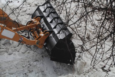 Büyük kovalı modern sarı traktör kardan yolu temizliyor, karları temizliyor, bahçede özel ekipmanlar var.