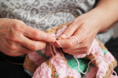 the age hands of a woman with knitting needles knit a product, grandmother's hobby clothes are made by hand, knitting a colored sweater
