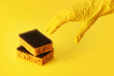 Sarı arka planda bulaşık yıkama süngeri, eldivenli bir el almak için uzanır, bir sarı renk şeması, tek renkli fotoğraf temizlik hizmetleri için arka plan, yatay yönelim