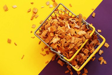 Natural calibrated alder chips for smoking on a yellow-purple background, convenient shopping concept, metal shopping basket full of wood shavings clipart