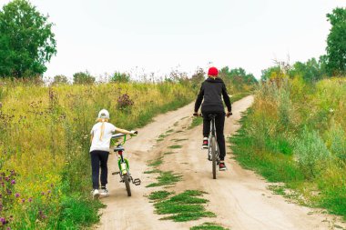 Ormanda kırsal bir yolda annesiyle bisiklete binen küçük bir kız. Spor aile hobisi. Sağlıklı yaşam tarzı.