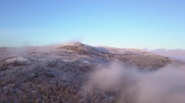 Alçak bulutların üzerinde, güneş ışınlarıyla aydınlatılan karla kaplı bir dağın üzerinde berrak bir gökyüzünde uçuyordu.