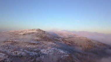 Alçak bulutların üzerinde, güneş ışınlarıyla aydınlatılan karla kaplı bir dağın üzerinde berrak bir gökyüzünde uçuyordu.