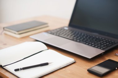 Ofis işyeri dizüstü bilgisayar, akıllı telefon ve ahşap masa üstünde defter