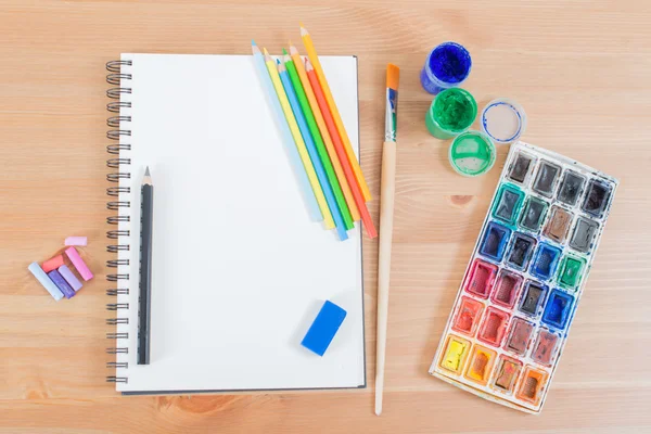 Top view of blank notebook or notepad and watercolour, pencils supplies on the wood background desk — Stockfoto