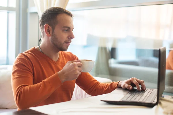 Joven guapo trabajando en el cuaderno, pensando, mientras disfruta del café en la cafetería — Foto de Stock