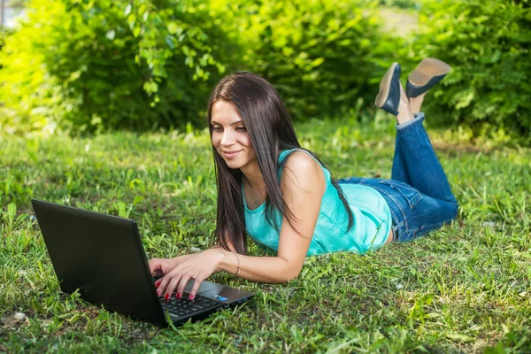 Jeune femme allongée sur l'herbe, en utilisant un ordinateur portable et en tapant — Photo