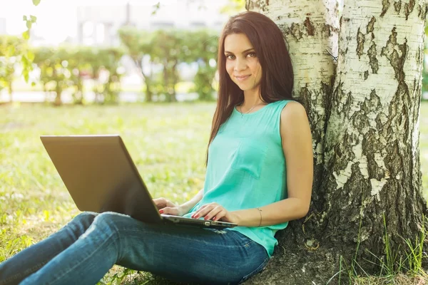 Jeune femme assise sur l'herbe, en utilisant un ordinateur portable et en tapant — Photo