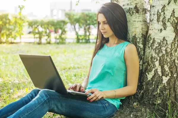 Jovem mulher sentada na grama, usando laptop e digitação — Fotografia de Stock