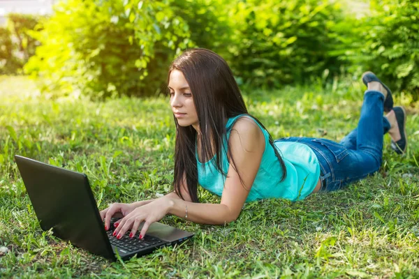 Jeune femme allongée sur l'herbe, en utilisant un ordinateur portable et en tapant — Photo