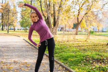 Genç bir kadın parkta egzersiz yapıyor. Sonbaharda dışarıda spor..