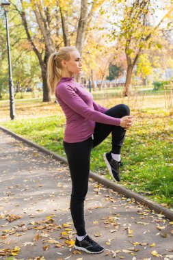 Genç kadın parkta esneme egzersizleri yapıyor. Sonbaharda dışarıda spor..