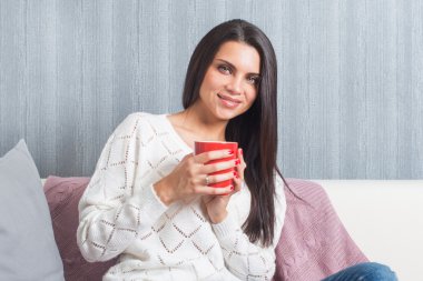 Onun elinde kırmızı bir kupa ile bir kadın gülümsüyor sittings kanepeye, kamera kanepe göz