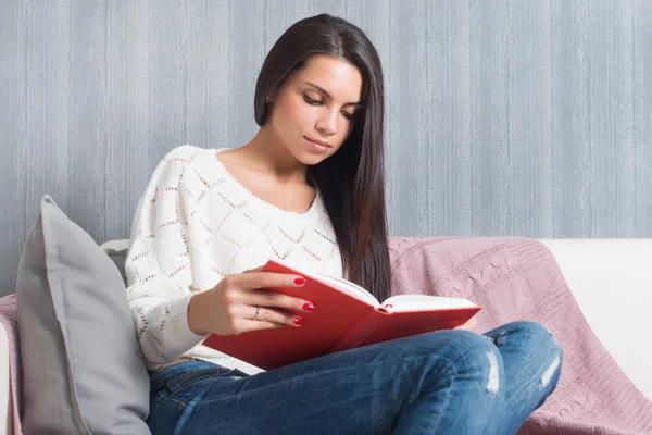 Jeune femme assise lire canapé livre à la maison — Photo