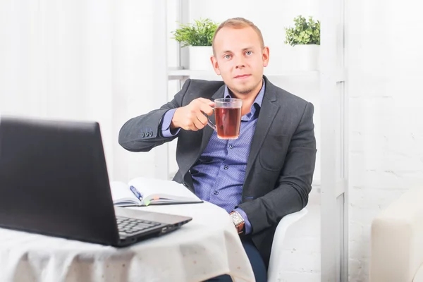 Empresario trabajando en la oficina, sentado en una mesa sosteniendo una taza y mirando recto . — Foto de Stock