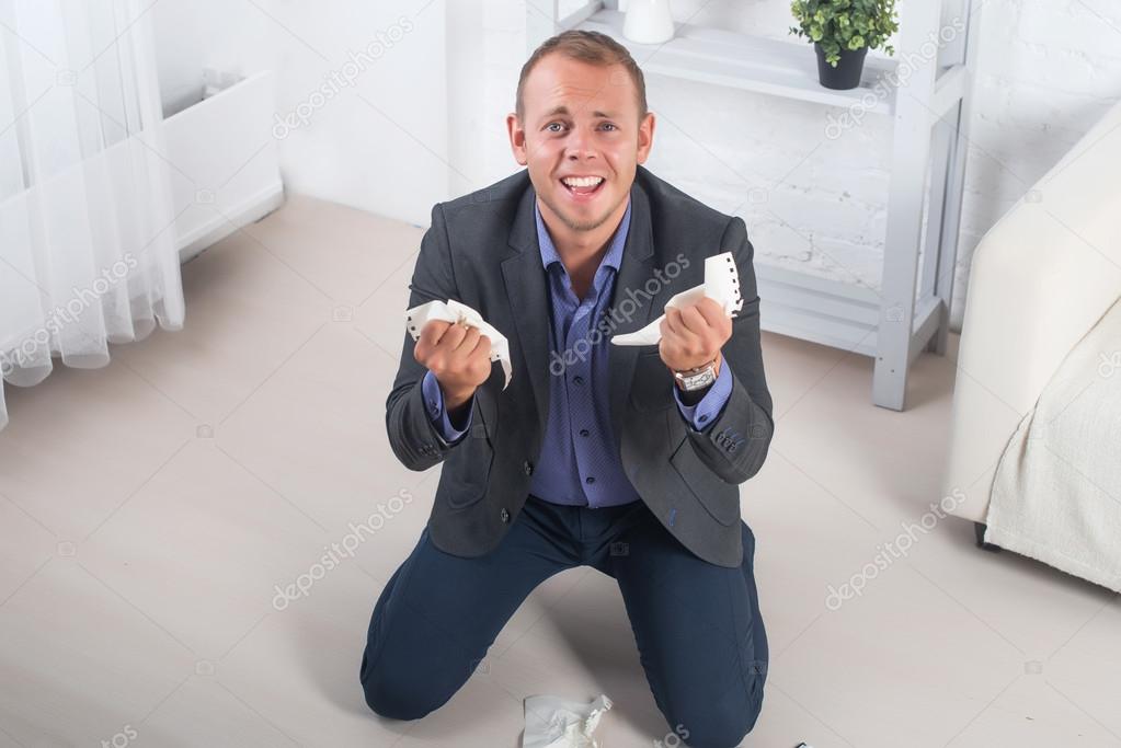 Young male businessman anger, hysterical kneeling on the floor, screaming and holding crumpled paper in his hands