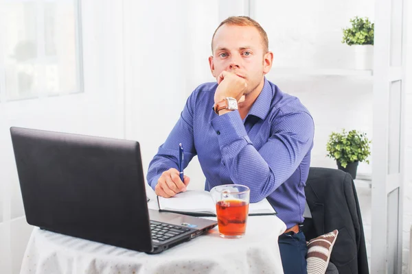 Empresário trabalhando no escritório, sentado à mesa com um laptop, olhando câmera — Fotografia de Stock