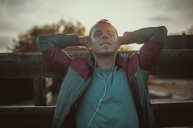 tired runner sitting, relaxing and listening to music  phone, eyes closed on a wooden pier, sport