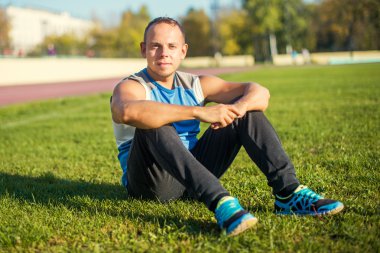 Çimenlerin üzerinde oturan bir çekici adam spor ve stadyumda aittir