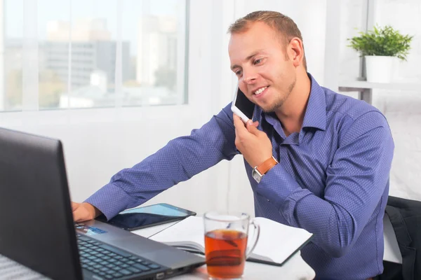 Joven hombre de negocios trabajando en la oficina, sentado en una mesa, hablando por teléfono — Foto de Stock