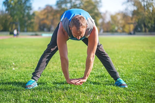 Deportista estirándose en el parque, haciendo ejercicios sobre hierba. Conceptos de fitness — Foto de Stock