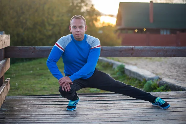 Homem esporte que se estende ao ar livre fazendo exercícios à noite ao pôr do sol. Conceitos de aptidão — Fotografia de Stock