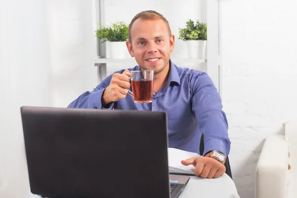 Homme d'affaires travaillant au bureau, assis à une table tenant la tasse et regardant droit . — Photo