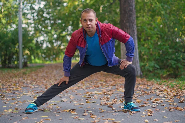 Hombre deportivo estirándose en el parque de otoño, haciendo ejercicios. Conceptos de fitness — Foto de Stock