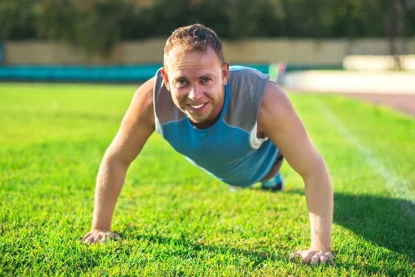 Hombre deportivo estirándose en el parque, haciendo flexiones en la hierba un día soleado. Conceptos de fitness — Foto de Stock