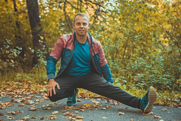 Hombre deportivo estirándose en el parque de otoño, haciendo ejercicios. Conceptos de fitness . — Foto de Stock