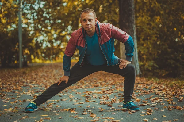 Homem do esporte que estica no outono do parque, fazendo exercícios. Conceitos de aptidão . — Fotografia de Stock