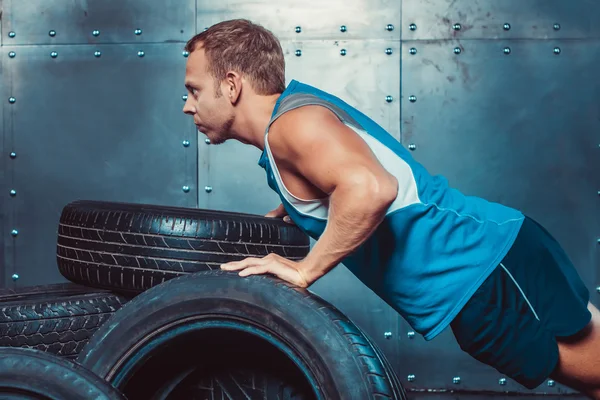 Hombre atlético entrena, empujado desde un neumático de coche mirando hacia adelante. con — Foto de Stock