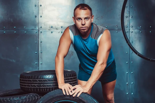 Sportsman se apoya en la máquina de neumáticos, mirando directamente a la cámara. Concepto de CrossFit, salud y fuerza — Foto de Stock