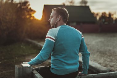 Çekici erkek spor akşam gün batarken Beach üzerinde oturan.