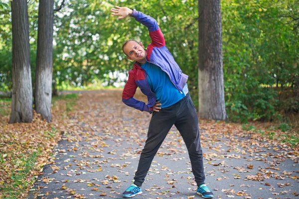 Hombre deportivo estirándose en el parque de otoño, haciendo ejercicios. Conceptos de fitness — Foto de Stock