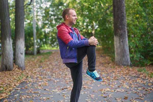 Hombre deportivo estirándose en el parque de otoño, haciendo ejercicios. Conceptos de fitness — Foto de Stock