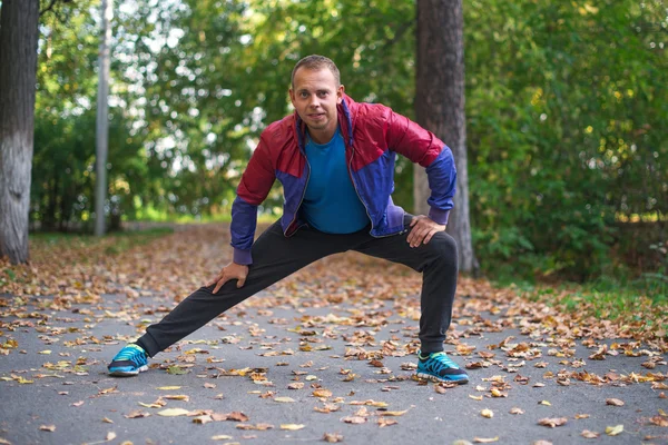 Hombre deportivo estirándose en el parque de otoño, haciendo ejercicios. Conceptos de fitness — Foto de Stock