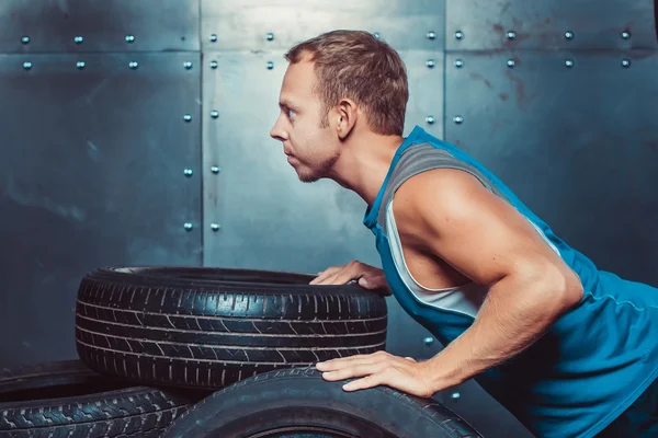 Hombre atlético entrena, empujado desde un neumático de coche mirando hacia adelante. concepto de salud y fuerza . — Foto de Stock