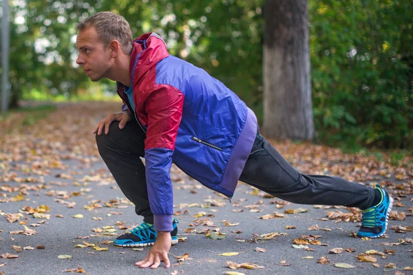 Hombre deportivo estirándose en el parque de otoño, haciendo ejercicios. Conceptos de fitness . — Foto de Stock