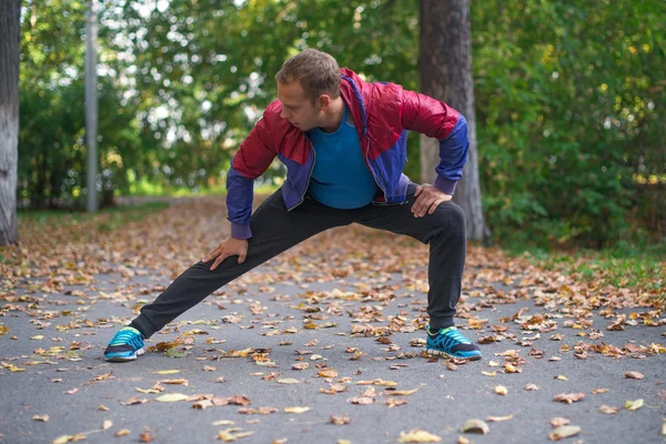 Hombre deportivo estirándose en el parque de otoño, haciendo ejercicios. Conceptos de fitness . — Foto de Stock