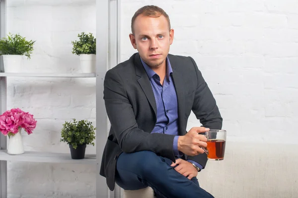 Hombre de negocios guapo sentado en el sofá en casa en la sala de estar, mirando a la cámara — Foto de Stock