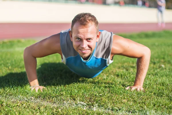 Hombre deportivo estirándose en el parque, haciendo flexiones en la hierba un día soleado. Conceptos de fitness . — Foto de Stock