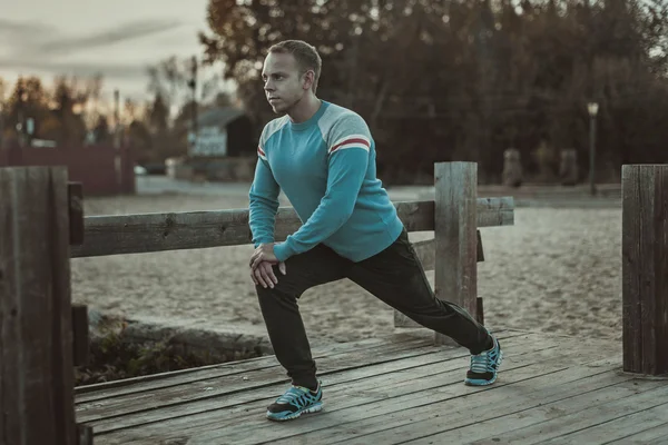 Hombre deportivo estirándose al aire libre haciendo ejercicios por la noche al atardecer. Conceptos de fitness . — Foto de Stock