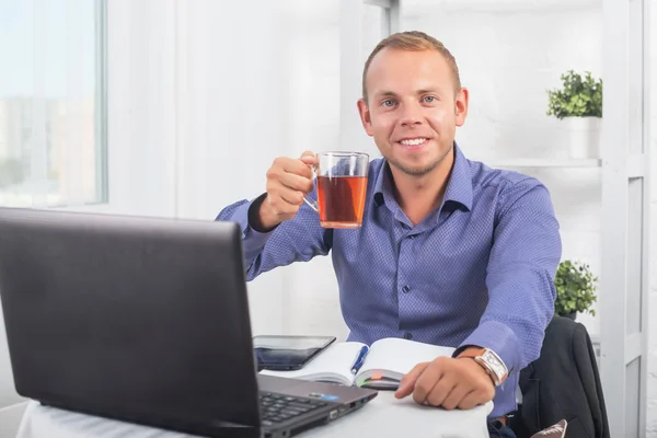 Empresário trabalhando no escritório, sentado a uma mesa segurando copo e olhando em linha reta . — Fotografia de Stock