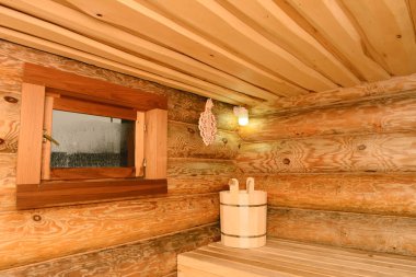 Interior of a Russian wooden bathhouse with a window, a shelf and a bucket