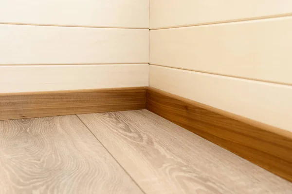 A corner of the room with wood-paneled walls, wooden skirting boards and a wooden floor