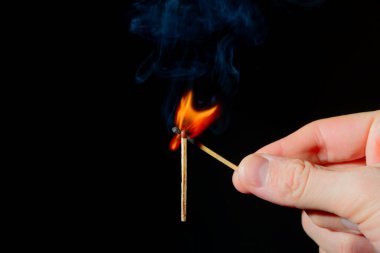 A burning match in his hand ignites a second match on a black background