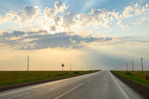 Evening landscape with the rays of the sun from under the clouds over the asphalt road in the field