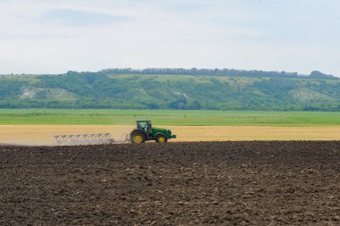 A tractor with a plow plows the land on a summer day