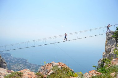 Turistler dağdaki uçurumun kenarındaki asma köprü boyunca yürürler.
